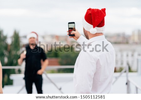 Christmas, celebration party, holiday, fun. Happy young man in Santa cap taking pictures of his friend celebrating New Year