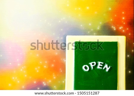 Close up of a green with yellow "OPEN" chalkboard sign leaning against sparkle ,bright with colorful background.