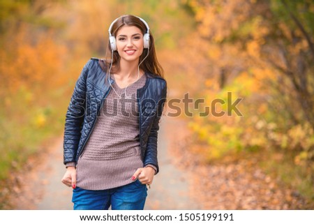 A portrait of a beautiful young woman walking in an autumn forest and listening to music. Lifestyle, autumn fashion, beauty. 