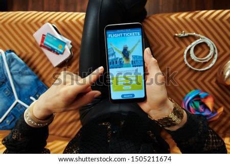 elegant housewife sitting on sofa in the modern living room booking airplane tickets online on a smartphone.