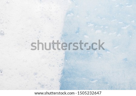 White foam on blue water top view background. Soapy liquid with white bubbles macro. Mousse texture, snow-white froth. Shower gel foam closeup. Household washing liquid, detergent dissolving in water