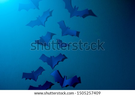 Halloween photo of blue paper bats flying up on dark blue background.