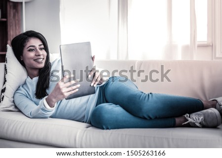 Young girlfriend photographing. Appealing dark-haired female making photo of herself with her tablet while lying on the couch