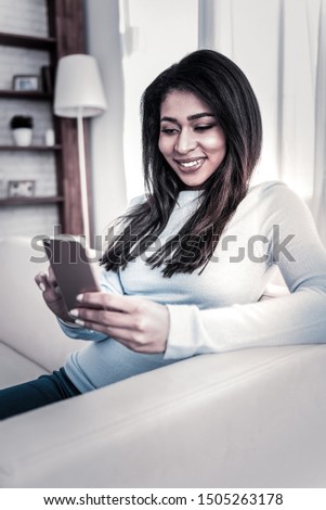 Smile on face. Attractive African American girl playing with her mobile phone while chilling at home