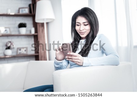 Cheerful appealing woman. Smiling dark-haired lady spending time with her phone having neat manicure