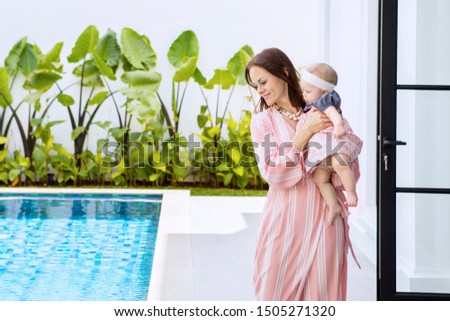 Picture of beautiful woman holding her baby while standing near the swimming pool