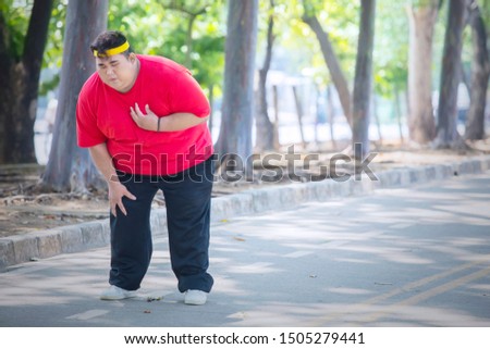 Picture of young obese man having heart pain after running in the park while standing on the road