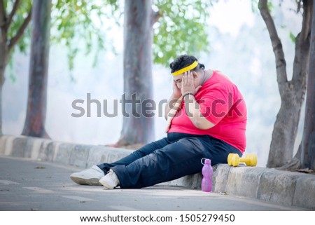 Picture of young fat man looks sad after exercise while sitting in the park