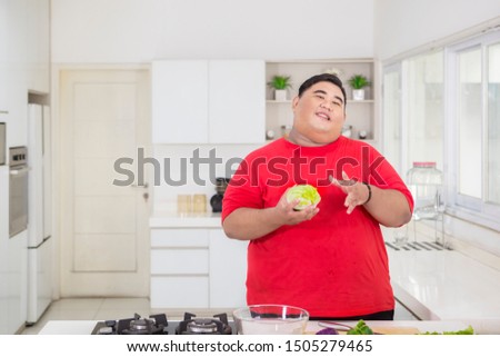 Picture of young fat man holding a cabbage while preparing to make a tasty salad in the kitchen