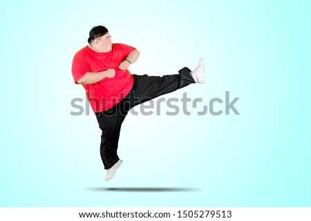 Picture of overweight man wearing sportswear while performing a kick in the studio