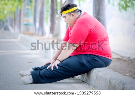 Picture of obese man looks tired after running in the park while sitting on the road. Shot in the park