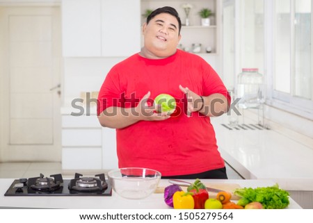 Picture of obese man holding a cabbage while preparing to make a tasty salad in the kitchen