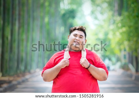 Picture of young obese man wearing sportswear while standing in the park
