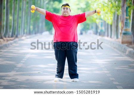 Picture of Asian fat man lifting two dumbbells while standing on the road