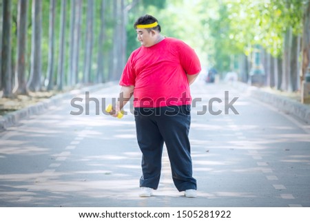 Picture of Asian fat man standing in the park while exercising with dumbbell 