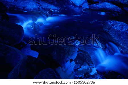 Blue rocks in stream with smooth flowing water at night. Long exposure photography