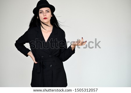 Concept portrait of a pretty brunette girl with long black hair in a hat and a business suit on a white background in studio. Standing right in front of the camera in various poses.