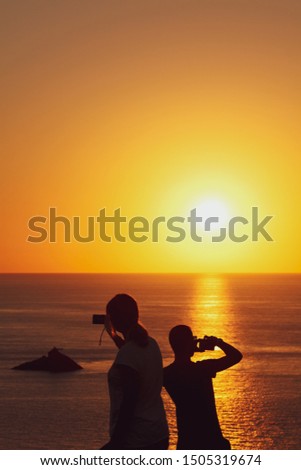 two people taking pictures of sunset against a beautiful warm light at capo sandalo in the Island of San Pietro, Sardinia