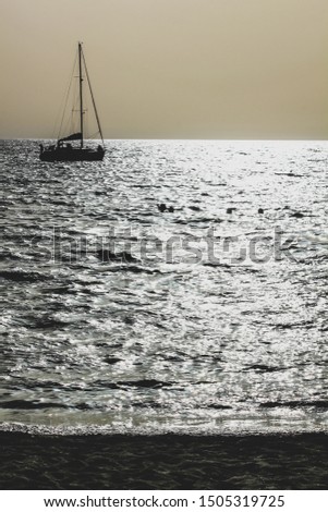 sailboat and three people bathing against light during sunset at the beach of caletta on the island of San Pietro in Sardinia