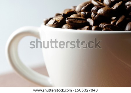 close up and selective focus of Coffee beans in a white cup on a wooden surface