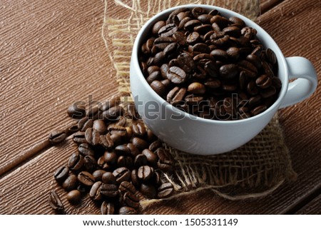Coffee beans in a white cup on a wooden surface