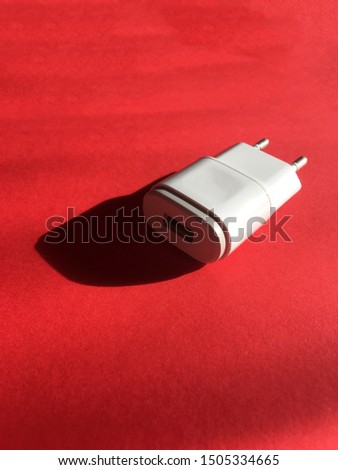 Close up to white color adapter plug on red paper pastel on background. Technology background view. Usb wall charger plug isolated on a red. Connector plug. Electrical adapter to USB port