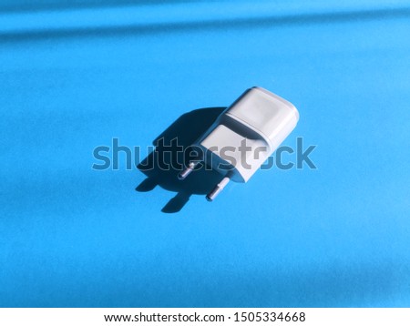 Close up to white color adapter plug on blue paper pastel on background. Technology background view. Usb wall charger plug isolated on a blue. Connector plug. Electrical adapter to USB port