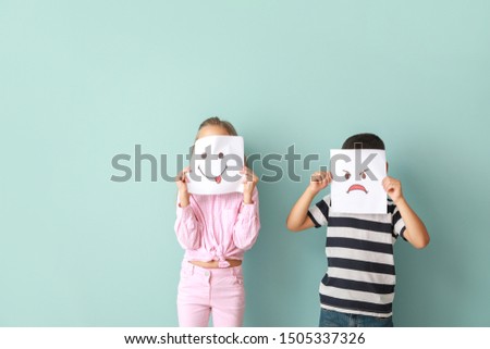 Little children hiding faces behind drawn emoticons on color background