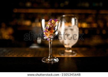 Close-up of an alcohol cocktail with flower and glass with ice on a wooden and metal bar counter