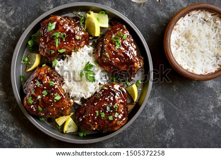 Sweet and spicy honey grilled chicken thighs with rice over dark stone background. Tasty food in asian style. Top view, flat lay