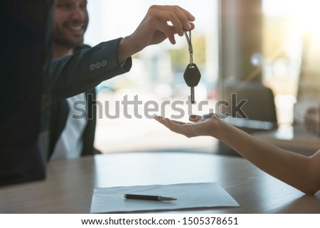 handsome man manager giving car keys after holding successful deal to his client at dealership office