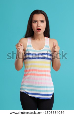 Brunette woman with long hair, dressed in striped shirt and black leggings, posing against blue studio background. Sincere emotions. Close-up.