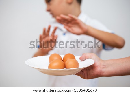Kid refusing to eat eggs. Egg Free Affected Allergy Banned Restriction. Young beautiful woman holding fresh egg at home with open hand doing stop sign with serious and confident expression