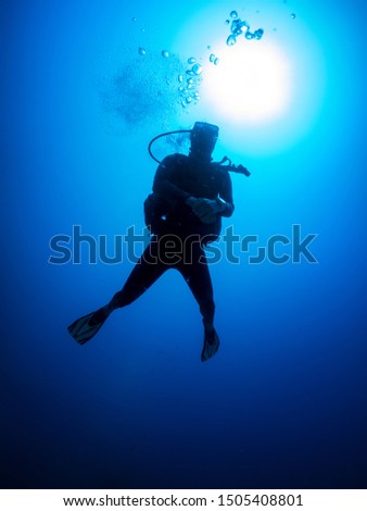 A silhouette of a scuba diver in the deep, blue sea against sunlight