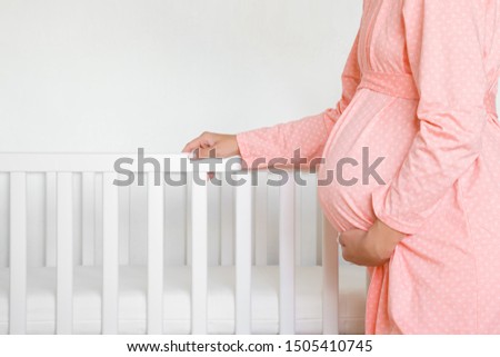 Pregnant woman in pink robe standing beside white crib for future baby. Waiting concept. Royalty-Free Stock Photo #1505410745