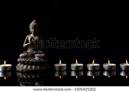 Statue of Buddha sitting in meditation, 
candle line With black copy space . Zen and meditation concept.