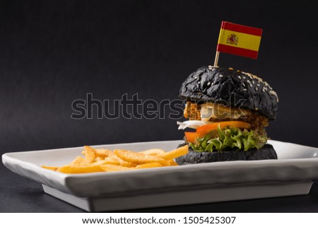 black hamburger with Spanish flag on top with French fried. black background