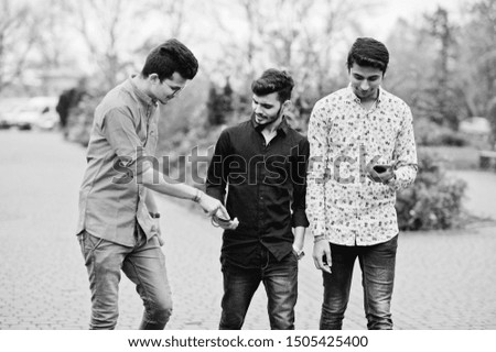 Three indian guys students friends walking on street and looking at mobile phone. Black and white photo.