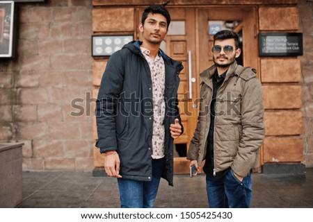 Two indian guys on jackets posed outdoor against door of pub.