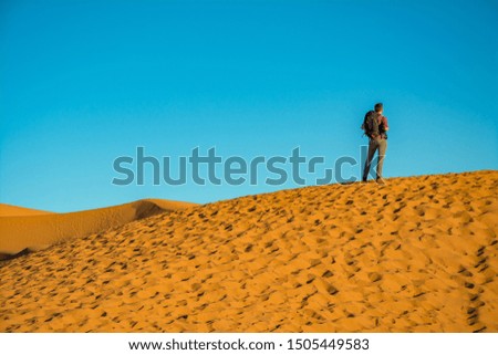 Young man standing on the dune and enoying the sunset on the Merzouga desert, Morocco