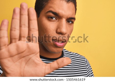 Young handsome arab man wearing navy striped t-shirt over isolated yellow background with open hand doing stop sign with serious and confident expression, defense gesture