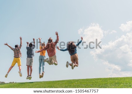 back view of multicultural kids jumping and gesturing against blue sky 