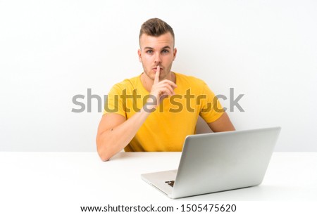 Young blonde man in a table with a laptop doing silence gesture