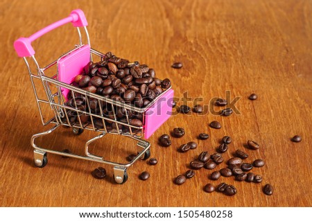  
Coffee beans in a shopping cart on a wooden background.                             