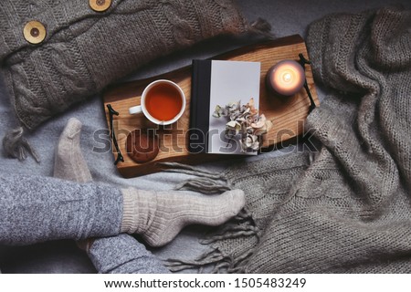 Cozy home with cup of tea with steam, blanket, book and candles. Hygge home interior