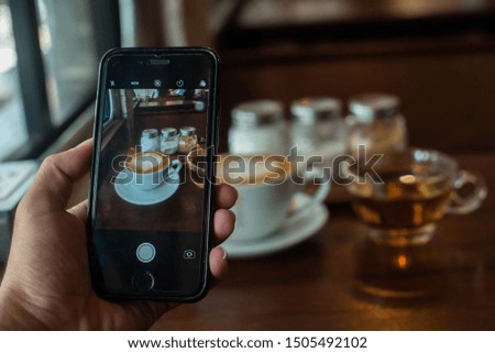 The phone is taking a picture of a cup of latte coffee