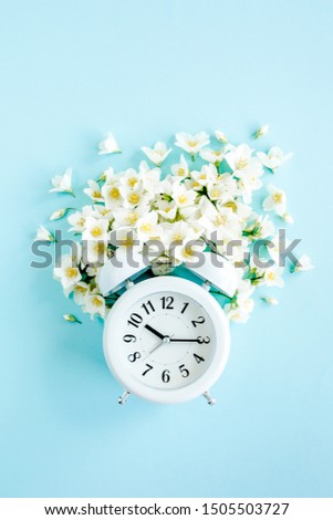 Composition-Summer time from Jasmine flower and clock, alarm on blue background. Flat lay, top view