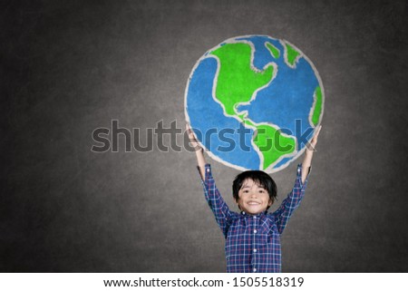 Picture of little boy smiling at the camera while lifting a globe drawn on the chalkboard