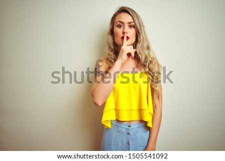 Young beautiful woman wearing yellow t-shirt standing over white isolated background asking to be quiet with finger on lips. Silence and secret concept.