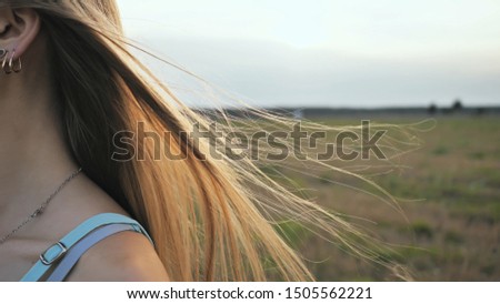Long hair of the brown-haired young girl scatter in the wind in the sunshine rays of the evening.